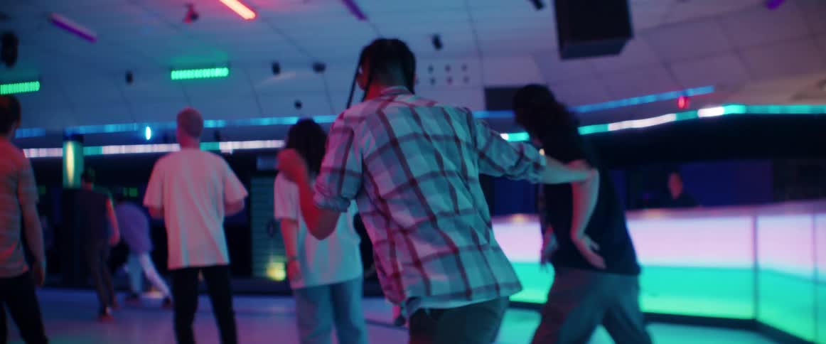 A young man skillfully glides and twirls as he roller skates around a crowded rink