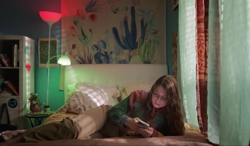 A young woman reclines on her bed while looking at her smart phone