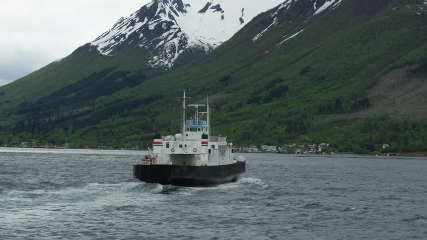 A ferry passing between snow capped mountains in Norwegian fjords