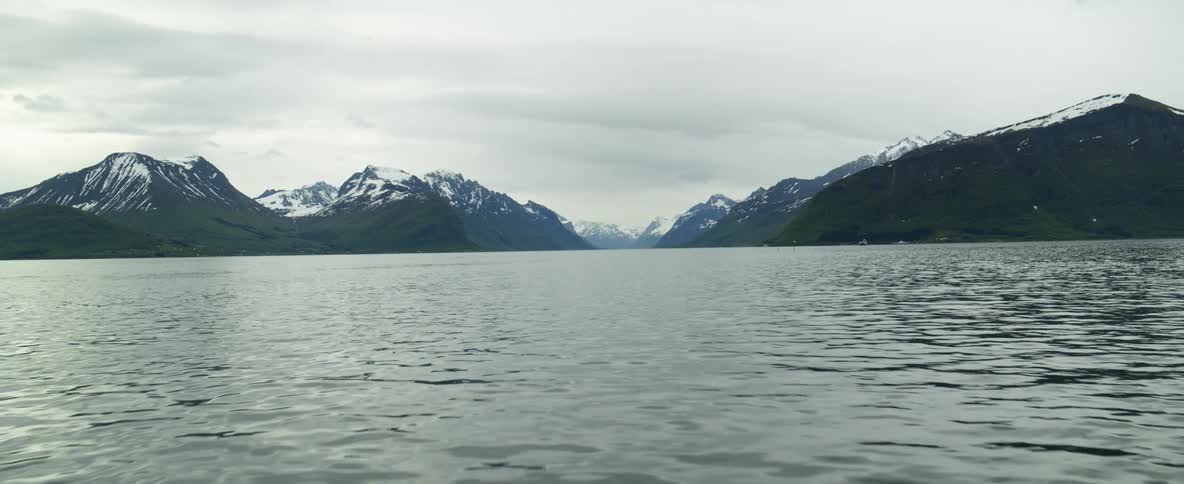 Snow dusted mountain ridges and peaks under a cloudy sky in Norway