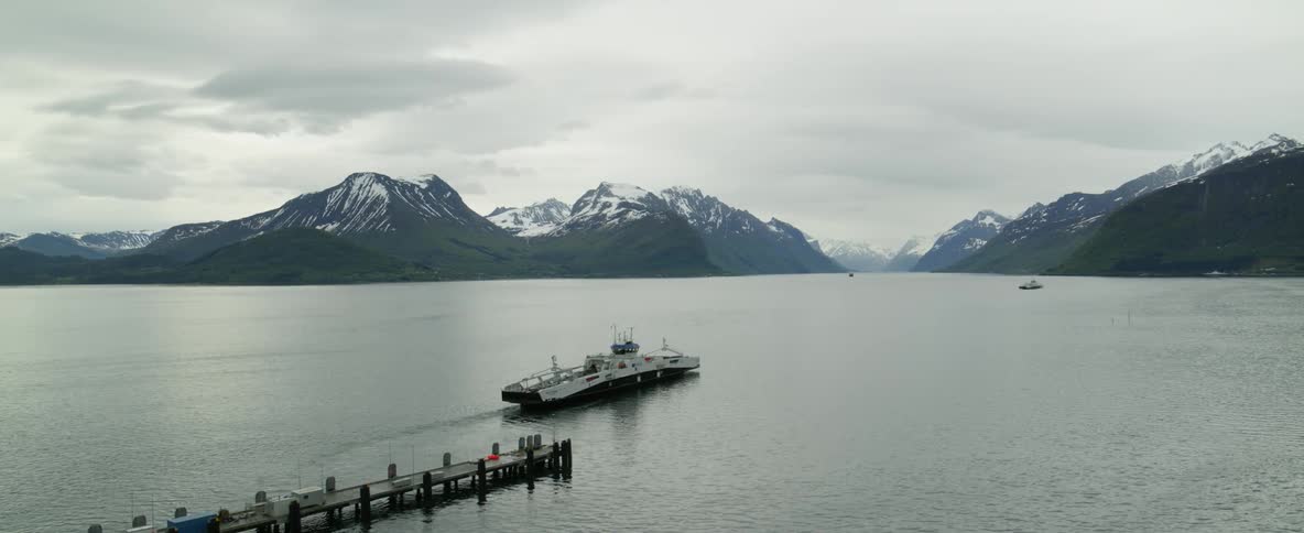 Aerial view of a ferry in Norwegian fjords with snowy mountains in background