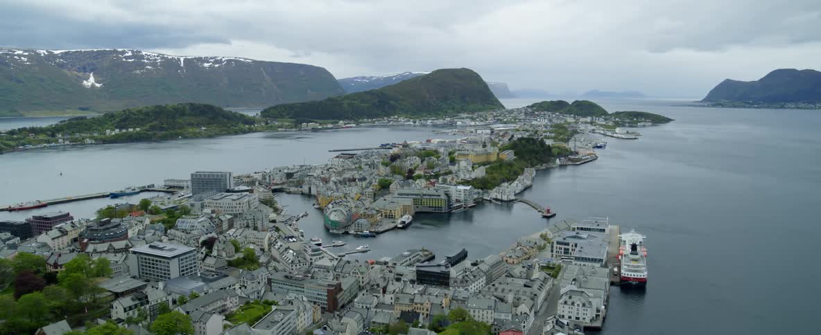 Aerial view of a ferry docked in Norwegian coastal town with mountains in background