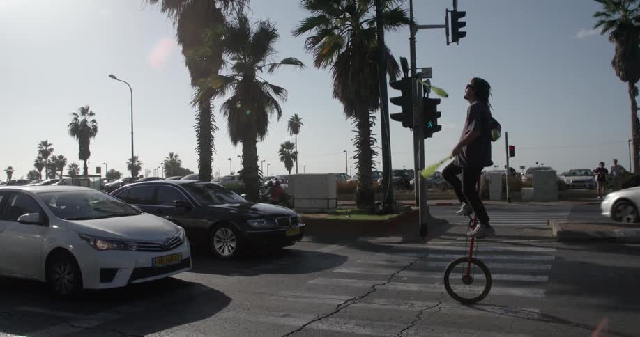 A man is in the street on a unicycle juggling