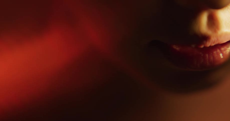 Close up of the red plump lips of a woman inside a dimly lit room