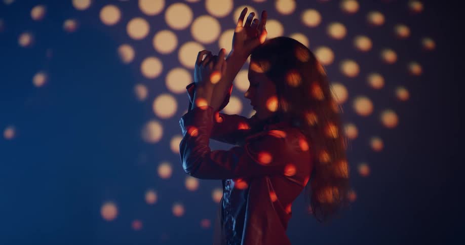 Young woman standing in front of a wall slowly changes pose under a pattern of dotted lights