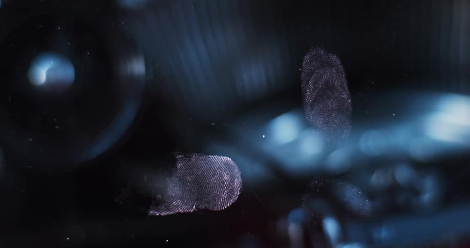 Close up of fingerprints over a pane of glass in front of a rotating typewriter under flashing red and blue lights