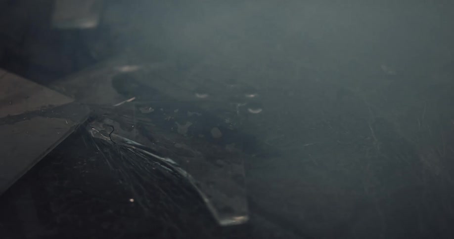 Smoke rolling over broken glass sprinkled with water on the ground of a dark room reflecting light