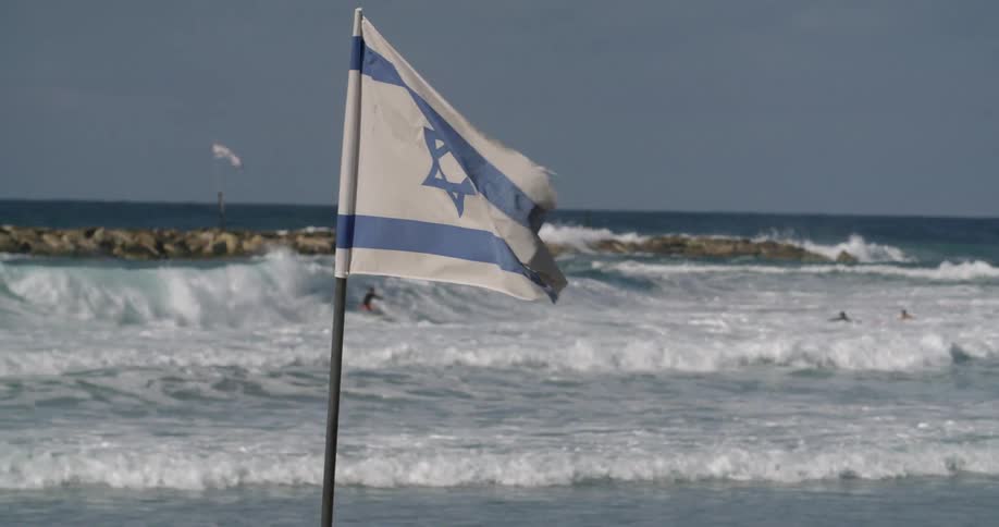An israeli flag billows on a beach