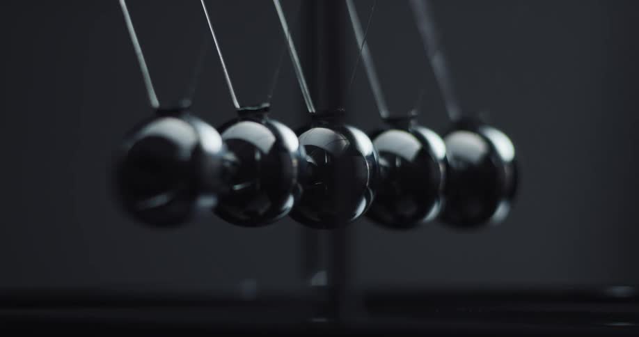 Metal balls are swinging back and forth in the darkness hitting each other in a newtons cradle