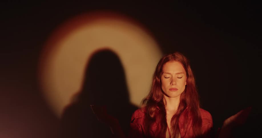 A woman takes a deep meditative breath standing on a stage in the spotlight