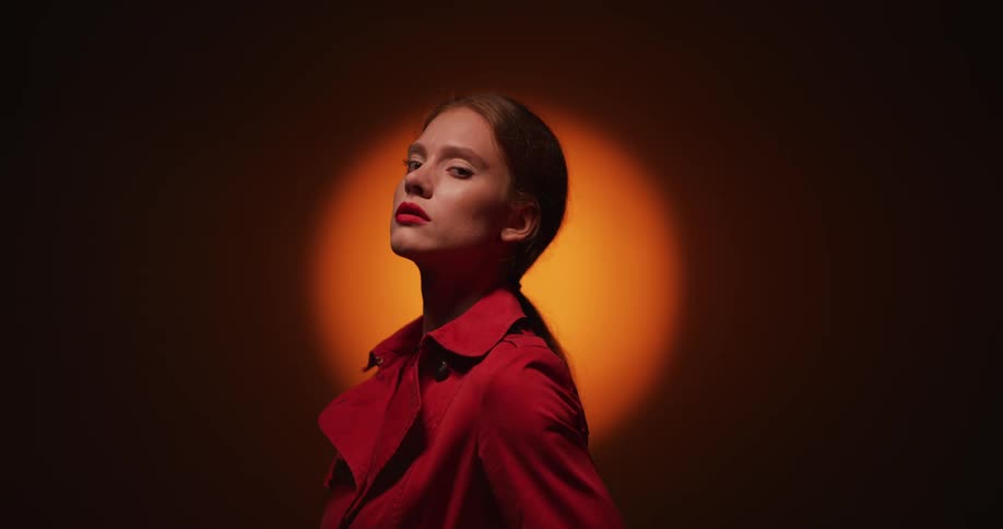 Female model with ponytail and brown coat stands in spotlight in room