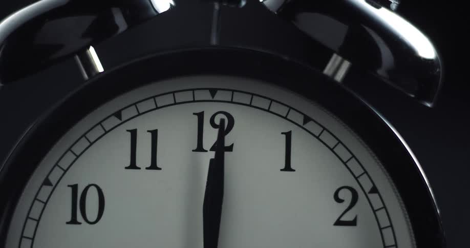 The hands of an alarm clock are moving just past twelve oclock
