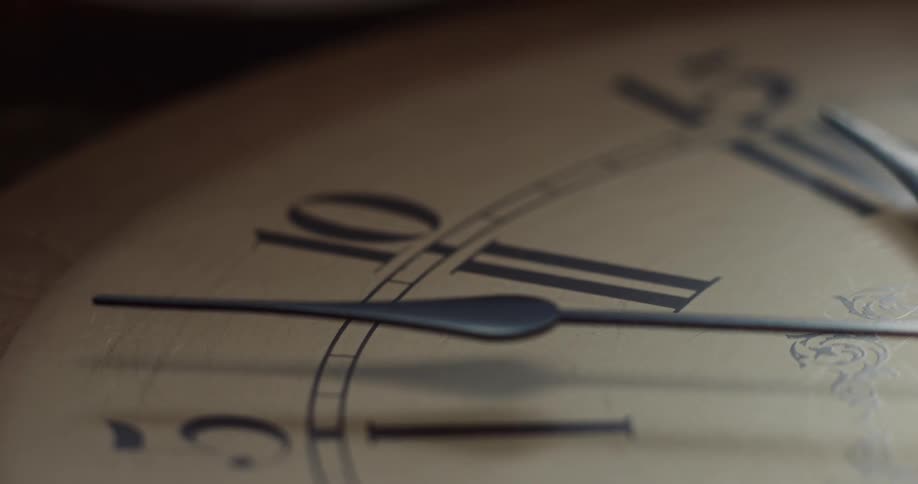 The hands of an analog clock cast a shadow on the clock face near the roman numerals