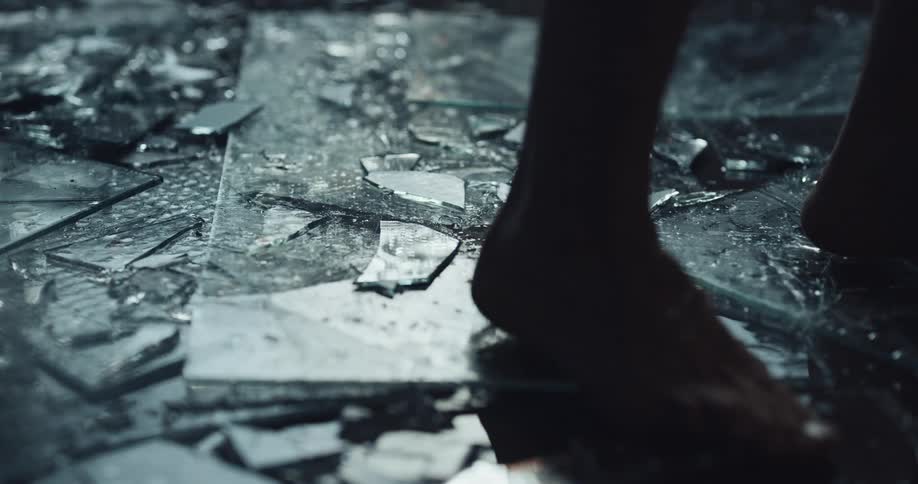 A person is walking barefoot across glass shards at night