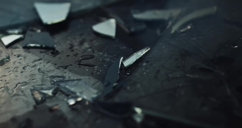Pieces of broken glass sprinkled with water on the ground of a dark room reflecting light