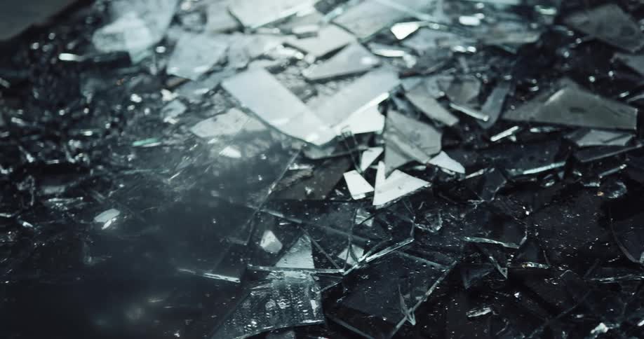 Pieces of broken glass sprinkled with water on the ground of a dark room reflecting light