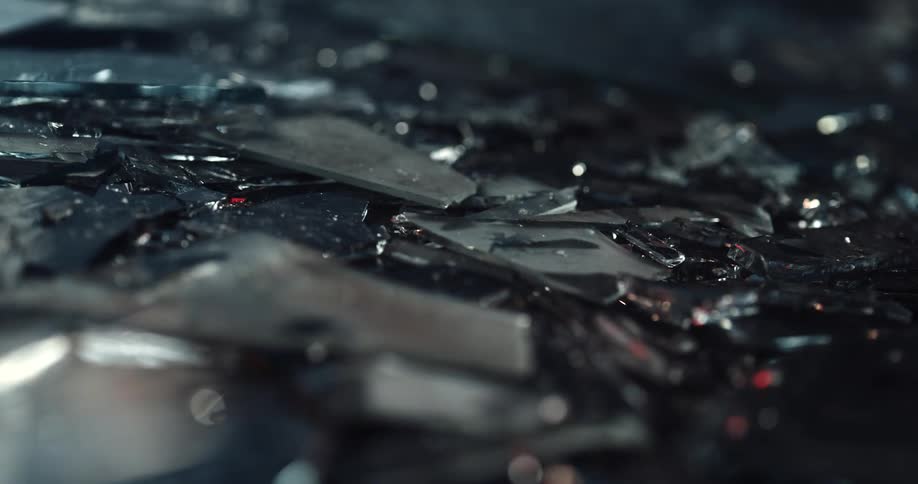 Pieces of broken glass sprinkled with water on the ground of a dark room reflecting light