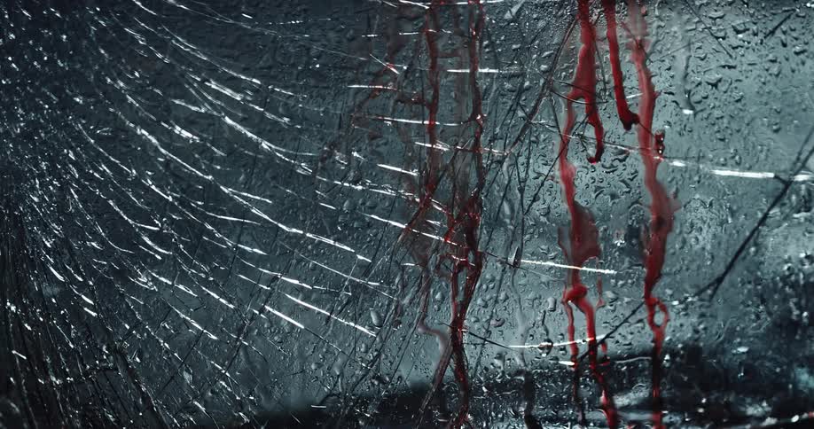 Blood drips and flows with rain down a cracked windshield at night