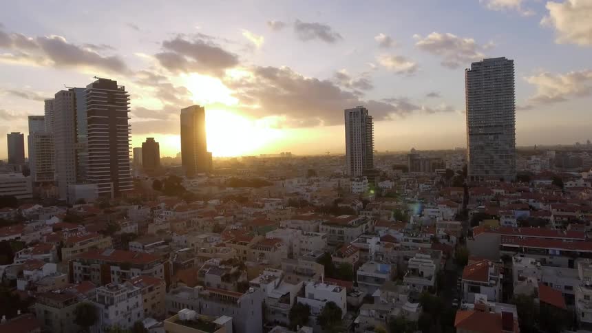 The sun sets behind city buildings and skyscrapers
