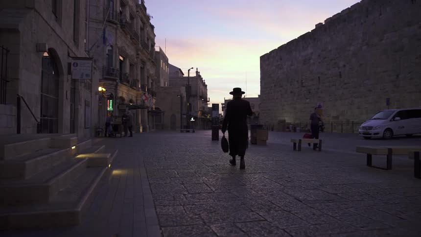A man in a hat walks down a dim street