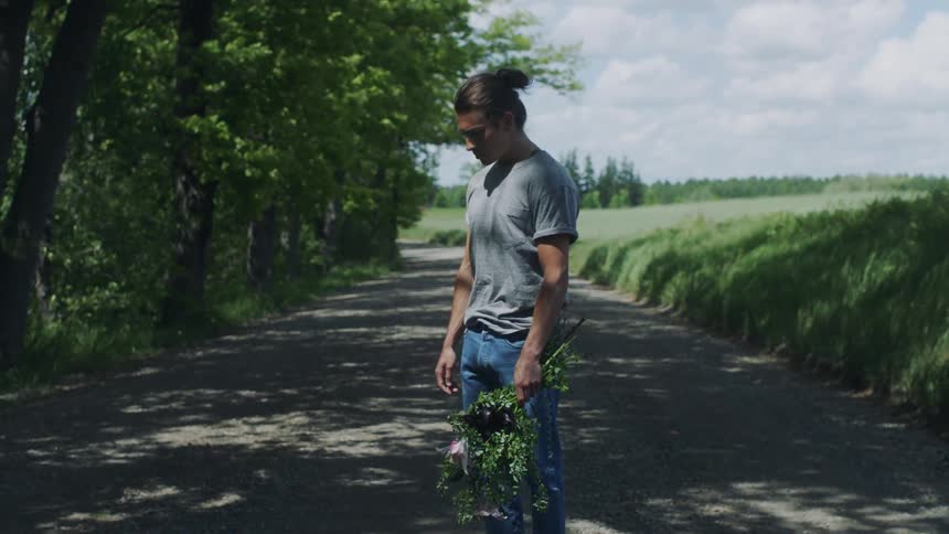 Disappointed man with bun gray shirt and jeans holds a bunch of flowers on country road in the countryside
