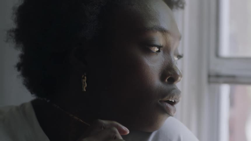 Woman with curly hair earrings and white shirt looks out the window