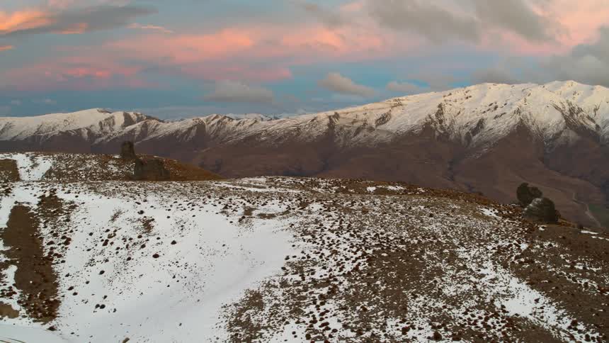 Snow covers tops of mountains under red tinted clouds