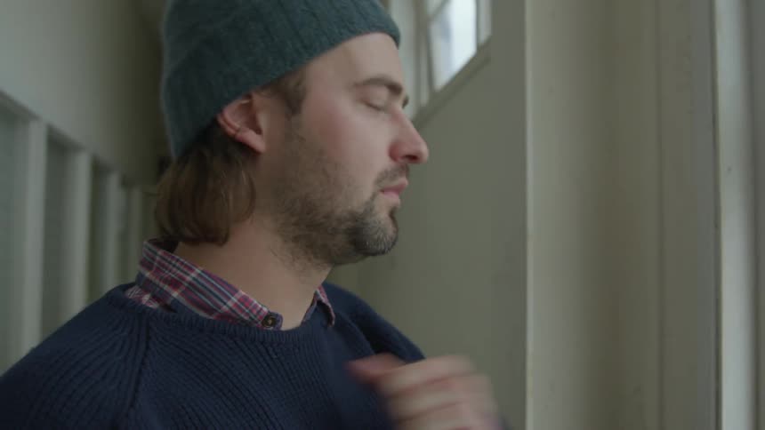 A man looking out the window coughs and punches his chest