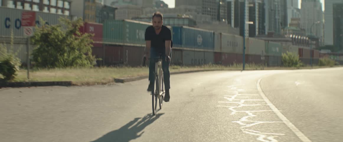 Man riding his bike down the street in a big city next to some shipping containers