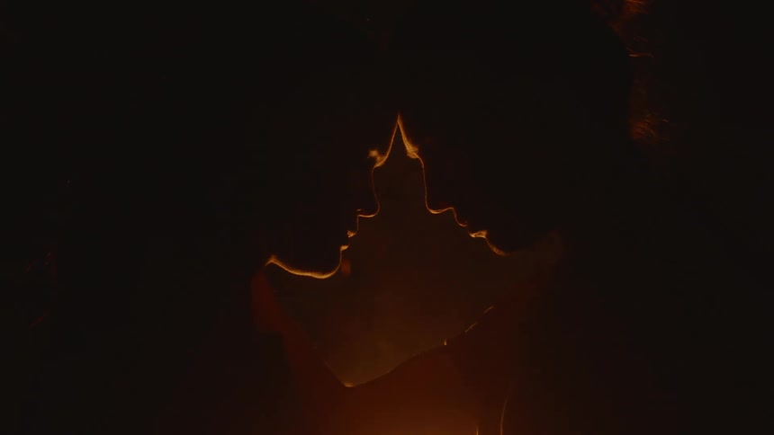 A couple moves closer together and touch heads in front of a bonfire