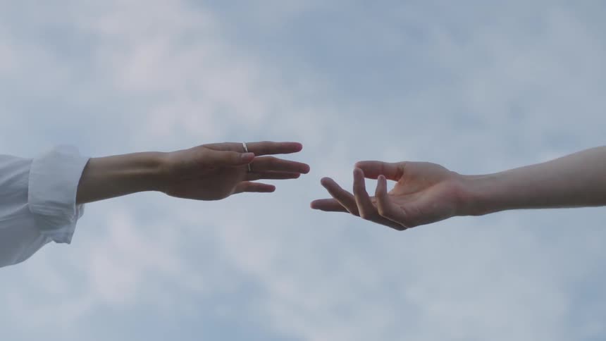 Two hands reaching for each other fingers extended against the sky