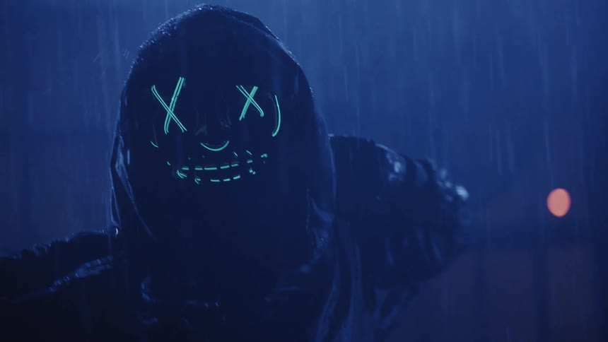 A dancer wearing a scarecrow mask and hoodie dances in the rain