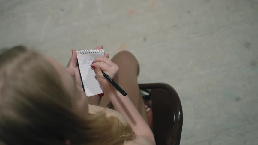 A girl sits in a chair and writes in a note pad