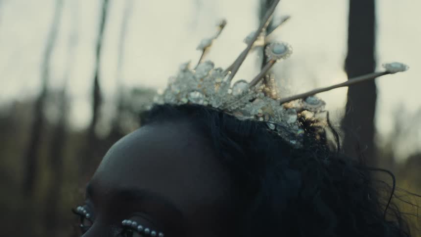 Sun shines onto head of woman wearing crystalline crown in woods