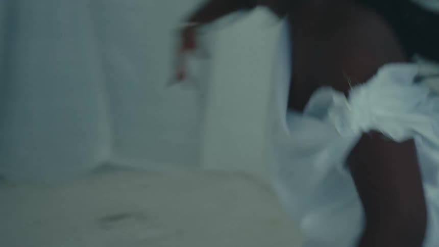 Close up of the torso of a dancing woman wearing a white toga inside a white room
