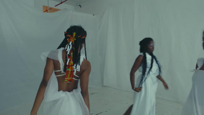 A group of women dance around a room in white dresses