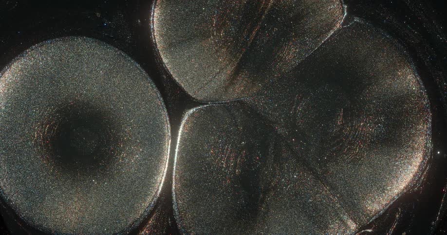 A surreal looking glittery fluid continuously flows upwards and spreads together