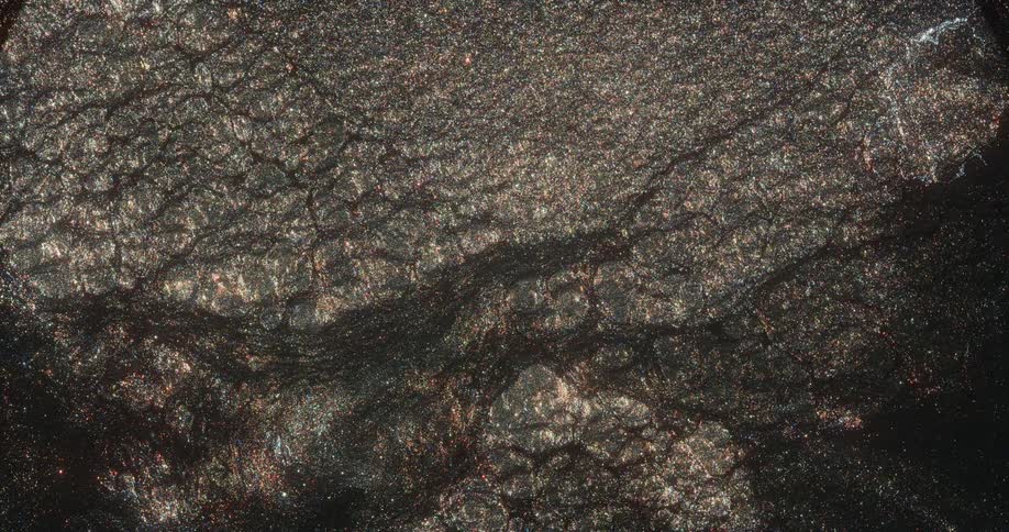 A gold and bronze glitter substance is spread across the darkness and comes to life and grows as it twinkles and moves