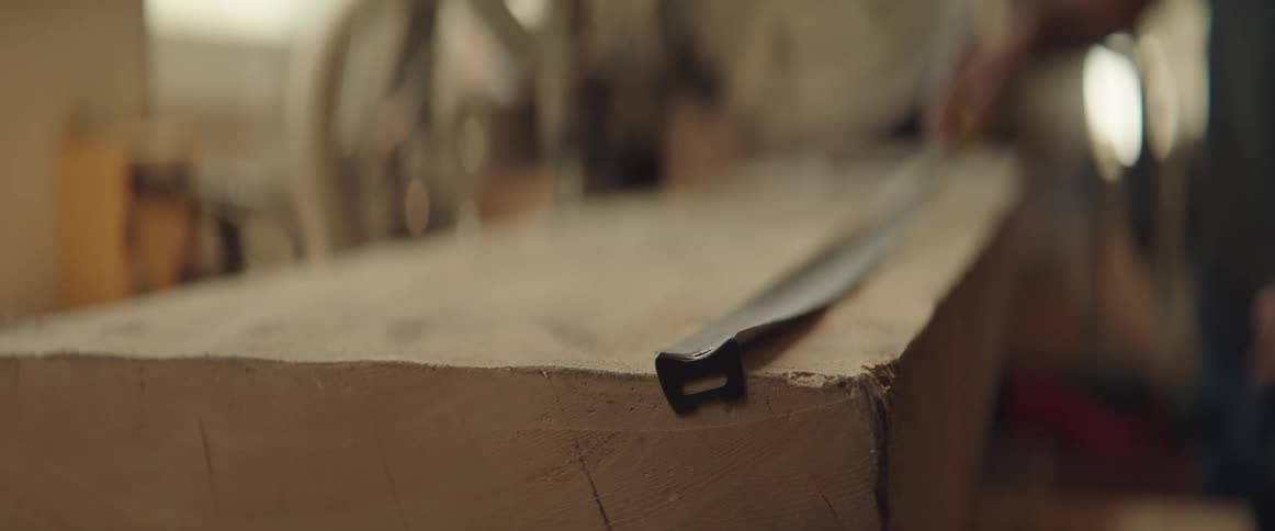 Man uses tape measure inside a workshop over a big plank of wood