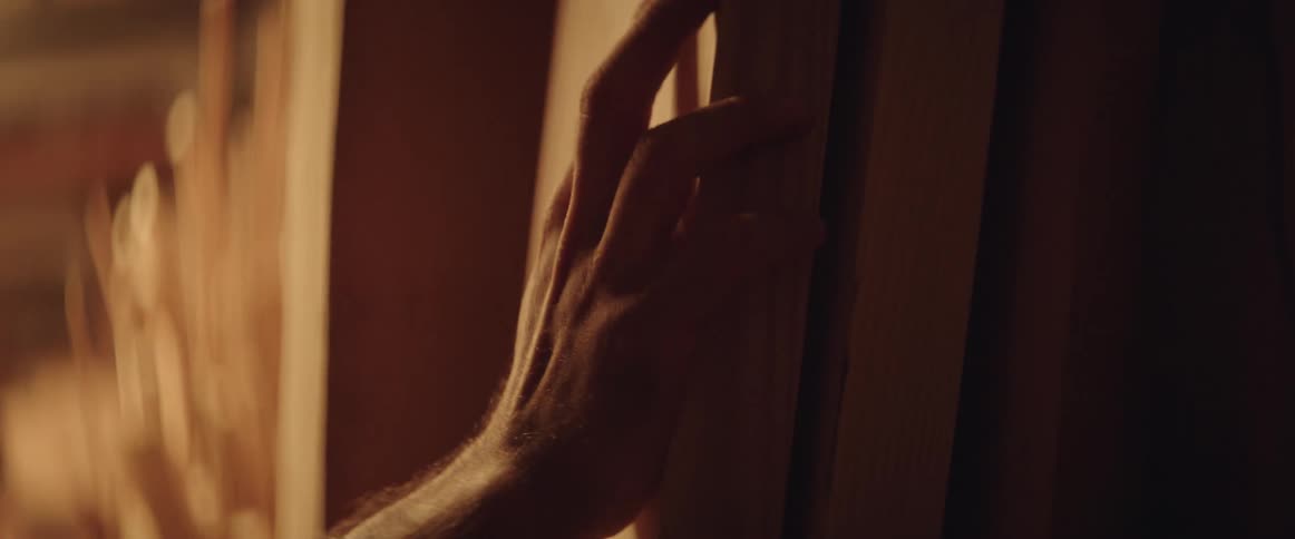 A man is running his hands down a wooden board that is leaning against the wall