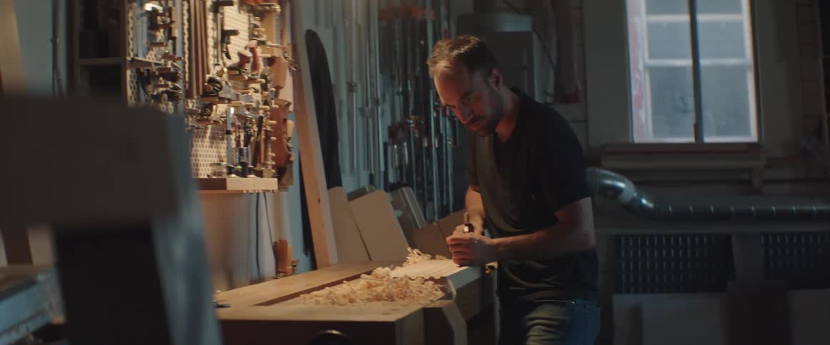 A male carpenter skillfully carves a piece of wood in his workshop