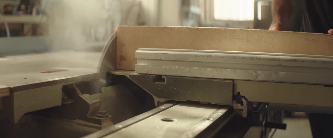 Man uses a circular saw to trim the side of a wooden board on a workshop