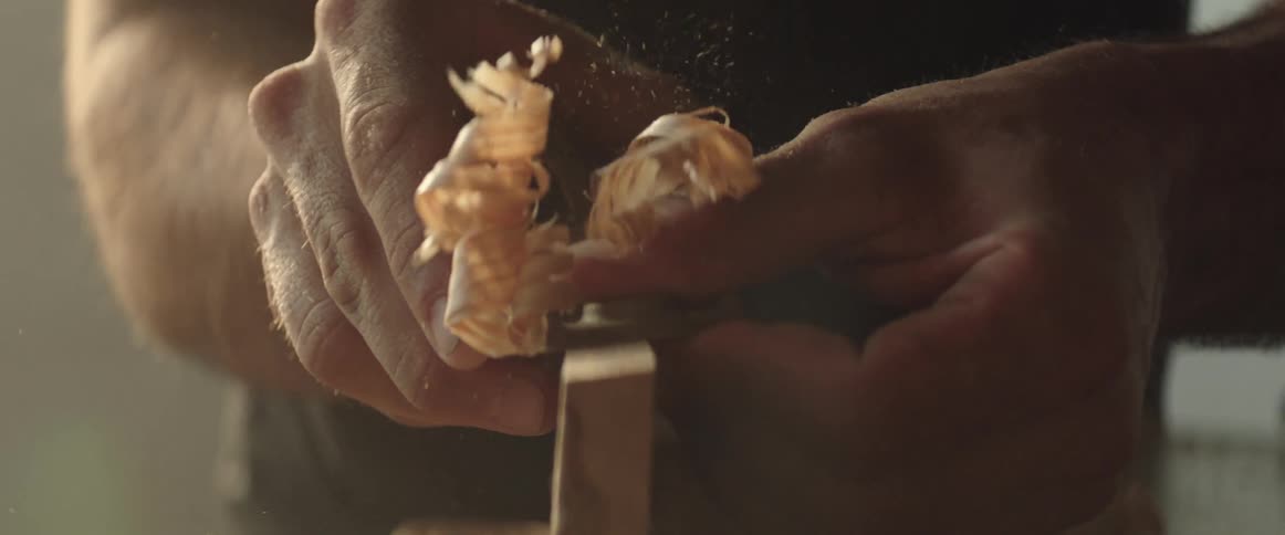 Wood shavings fly into the air as carpenter planes board