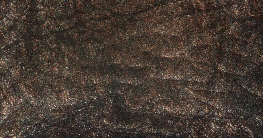 A sandy glittering metallic puddle of liquid is slowly shown having more liquid poured into it as the camera continues moving higher