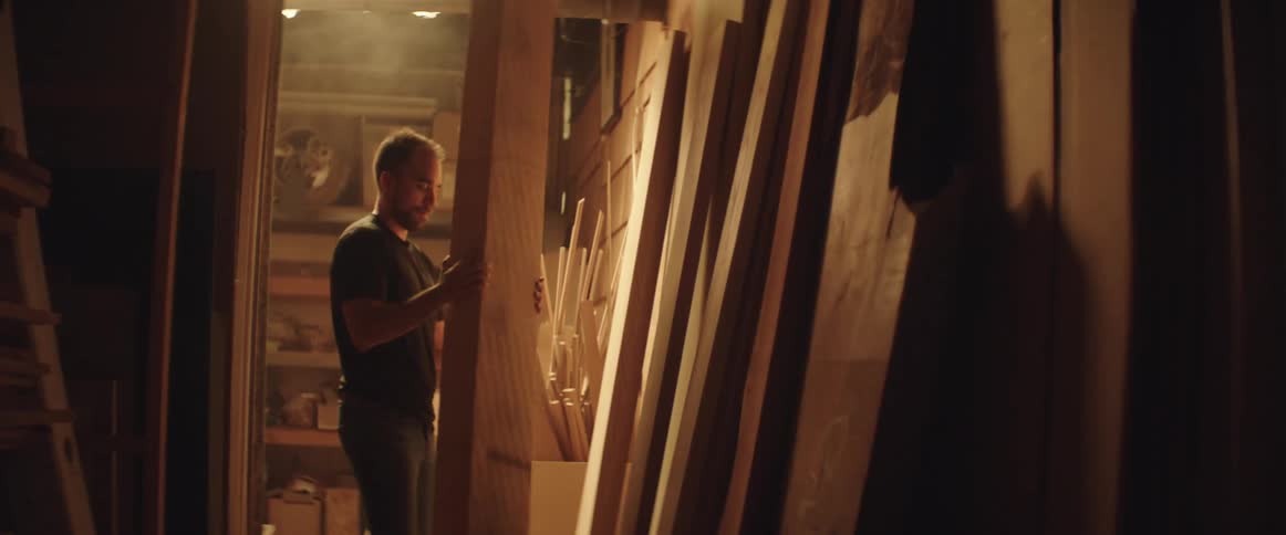A man picks up a large piece of wood and carries it