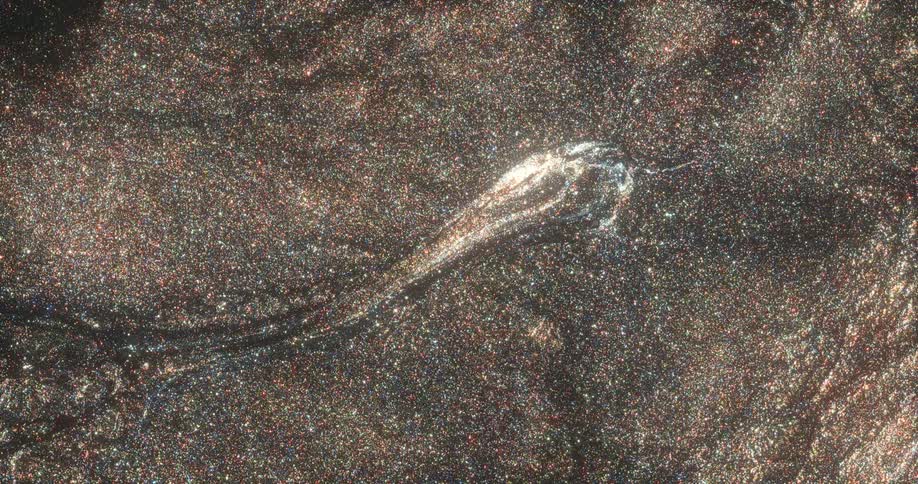A mass floating on a sparkling shimmering golden surface dissipates in a wave