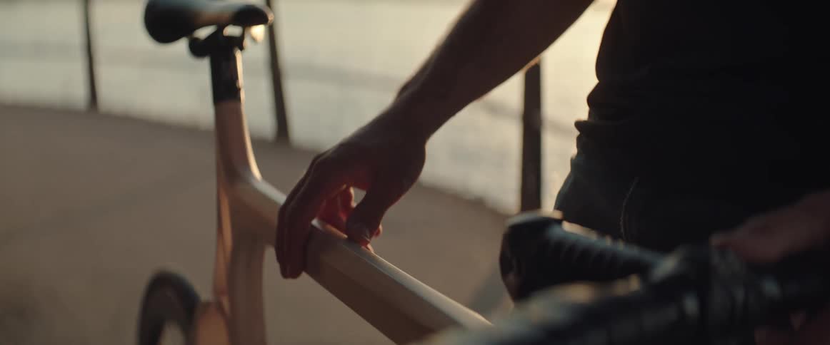 Man slides hand over the frame of a bicycle next to he ocean at sunset