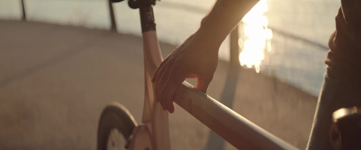 A hand of a man inspecting the finish of his bicycle by a large body of water at sunset