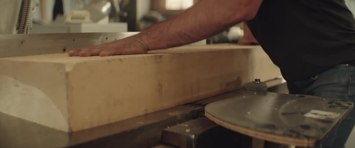 A man pushes a thick slab of wood through a jointer tool