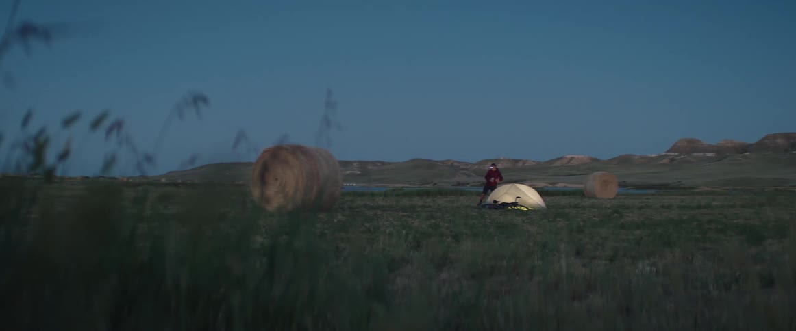 Man puts up tent next to bicycle in green field at dusk